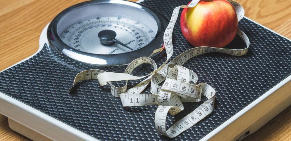 Báscula con cinta métrica y manzana que representa la evaluación del índice de masa corporal (IMC) y el peso saludable.