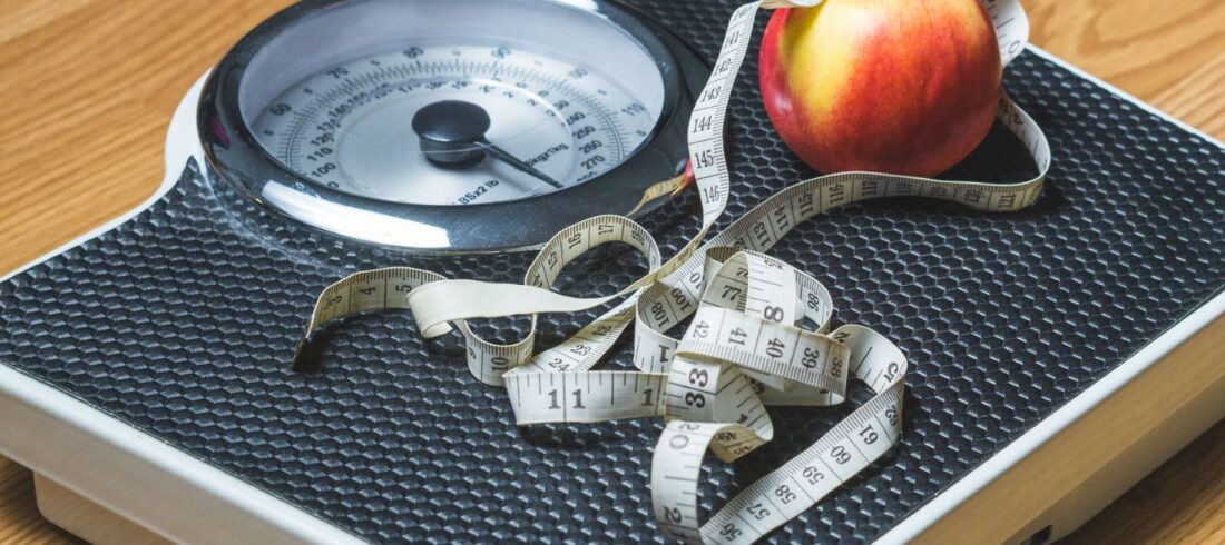 Báscula con cinta métrica y manzana que representa la evaluación del índice de masa corporal (IMC) y el peso saludable.