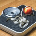 Báscula con cinta métrica y manzana que representa la evaluación del índice de masa corporal (IMC) y el peso saludable.