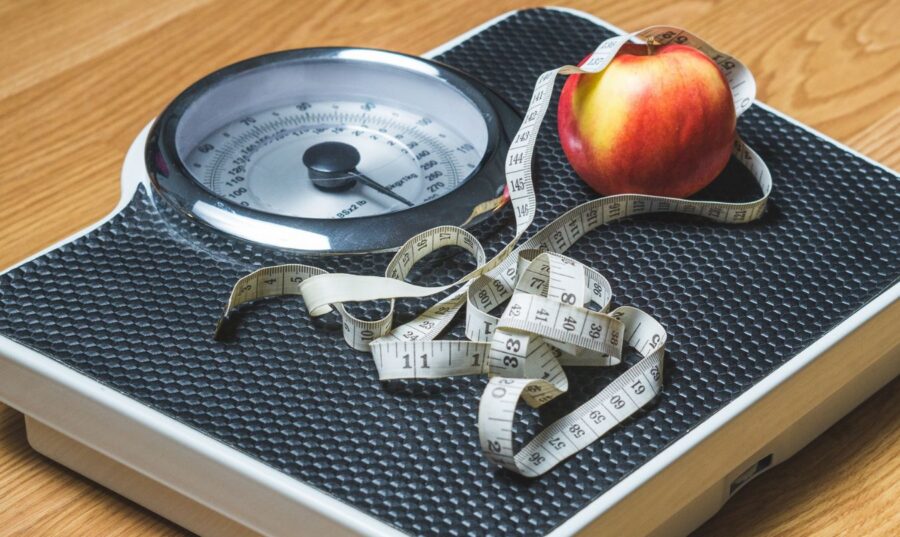 Báscula con cinta métrica y manzana que representa la evaluación del índice de masa corporal (IMC) y el peso saludable.