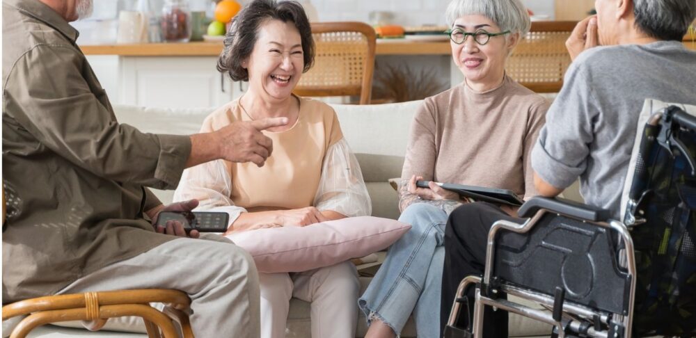 Grupo de adultos mayores conversando y sonriendo en una sala; uno de ellos utiliza una silla de ruedas.