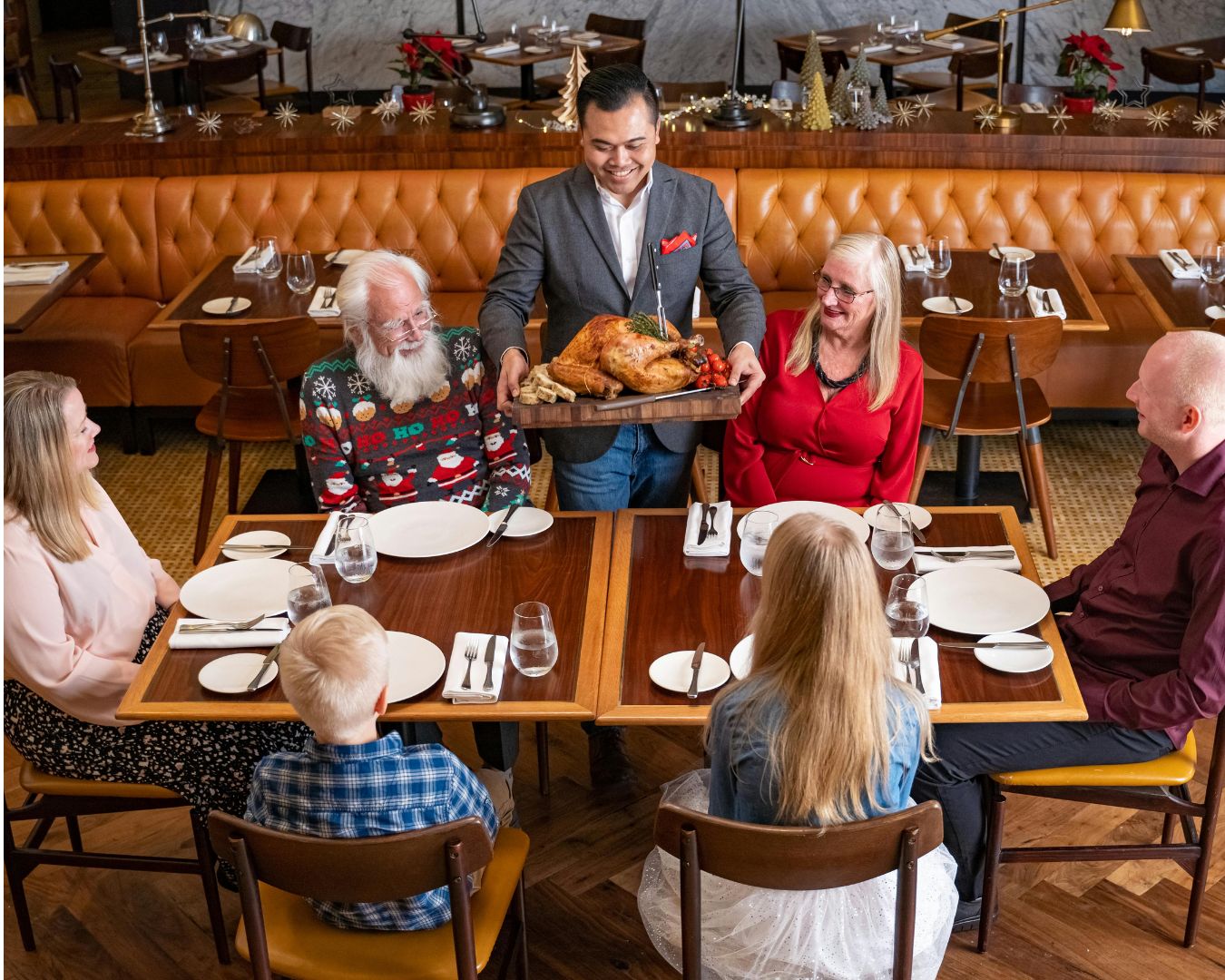 Adultos mayores comparten una comida con familiares y amigos en un restaurante mientras un mesero les sirve el plato principal.